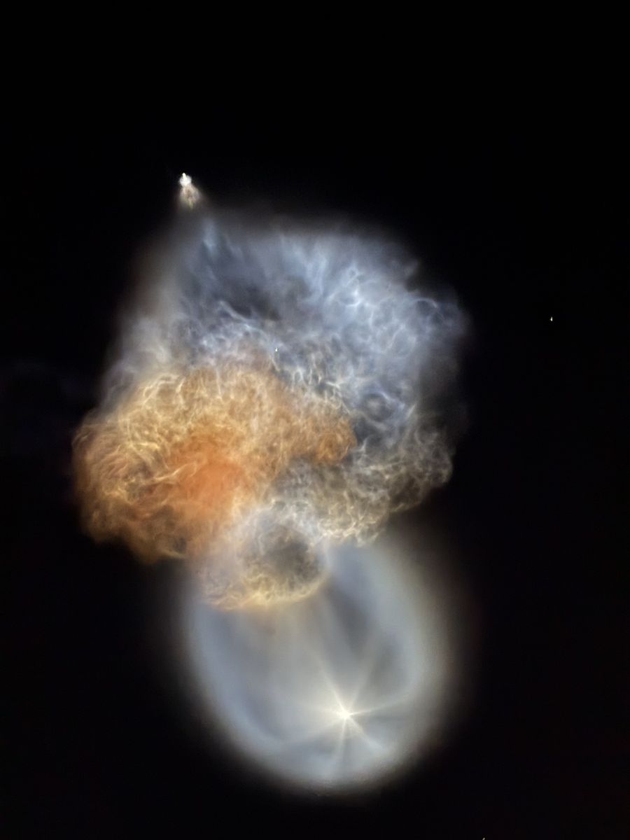 Falcon 9 exhaust plume glowing orange, blue and white against a dark sky, with a bright point at its upper end