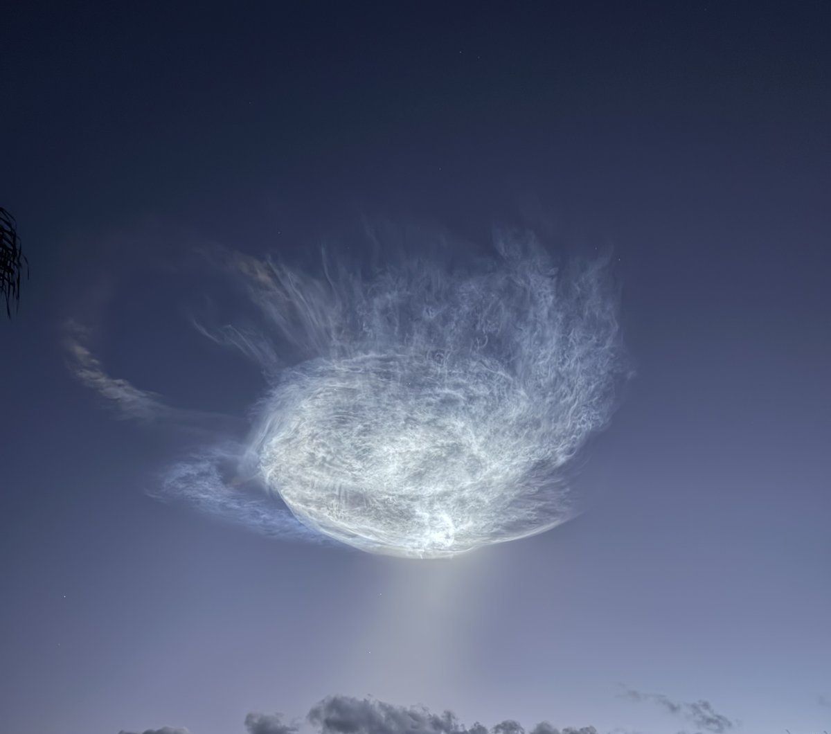 Swirling, glowing remnant of a rocket plume in a deep blue pre-dawn sky