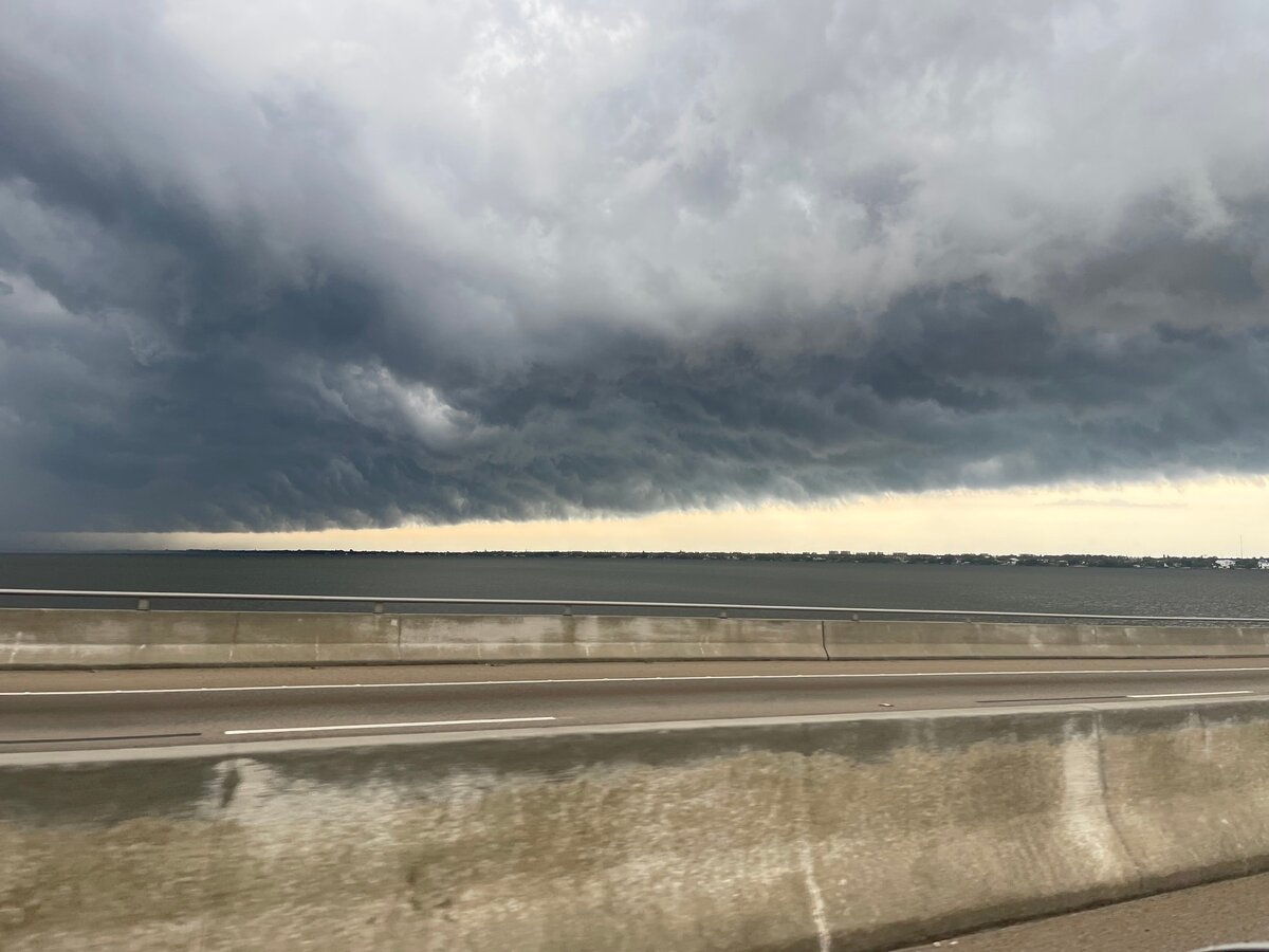 A long, low shelf cloud stretches across the Indian River with a strip of light below it, seen past causeway barriers