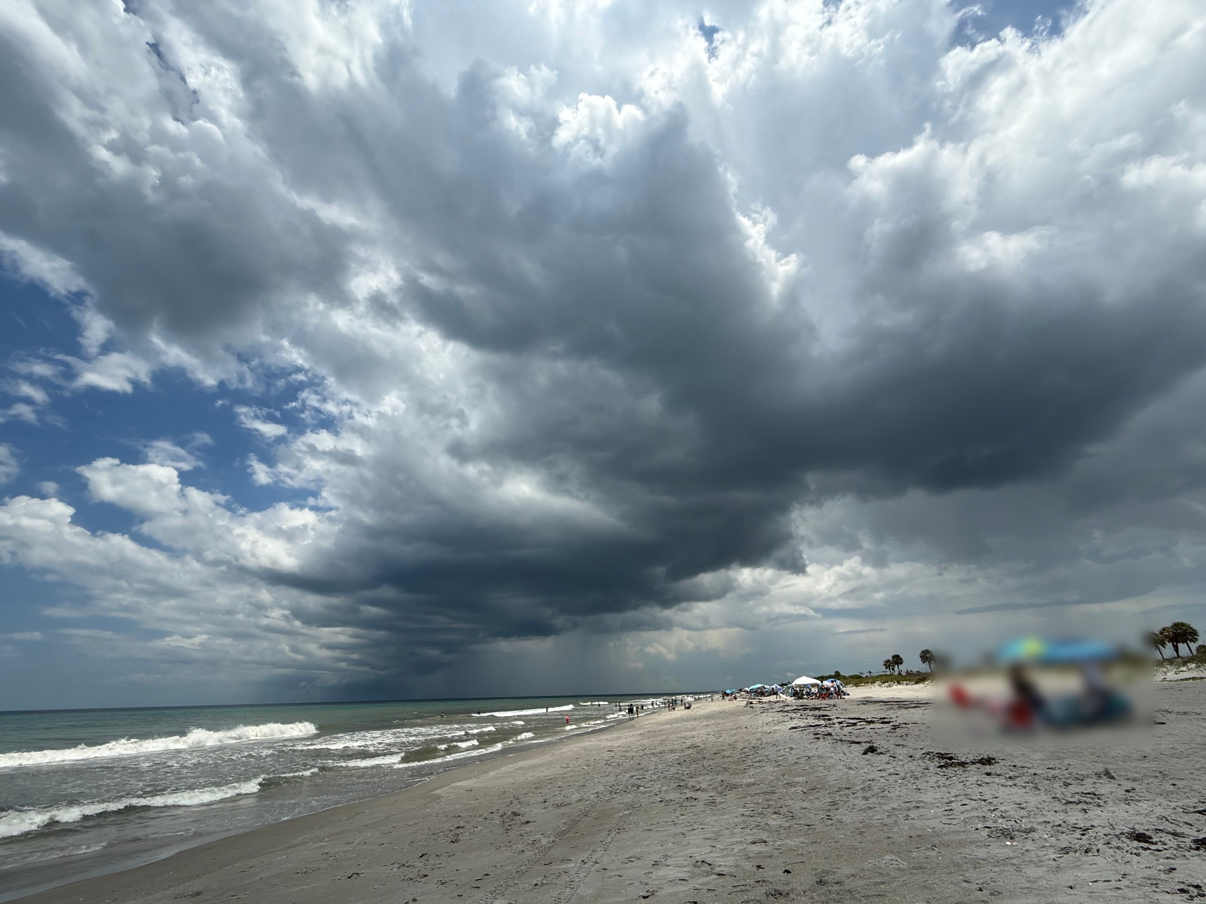 Towering gray storm clouds build over breaking surf and a sandy beach