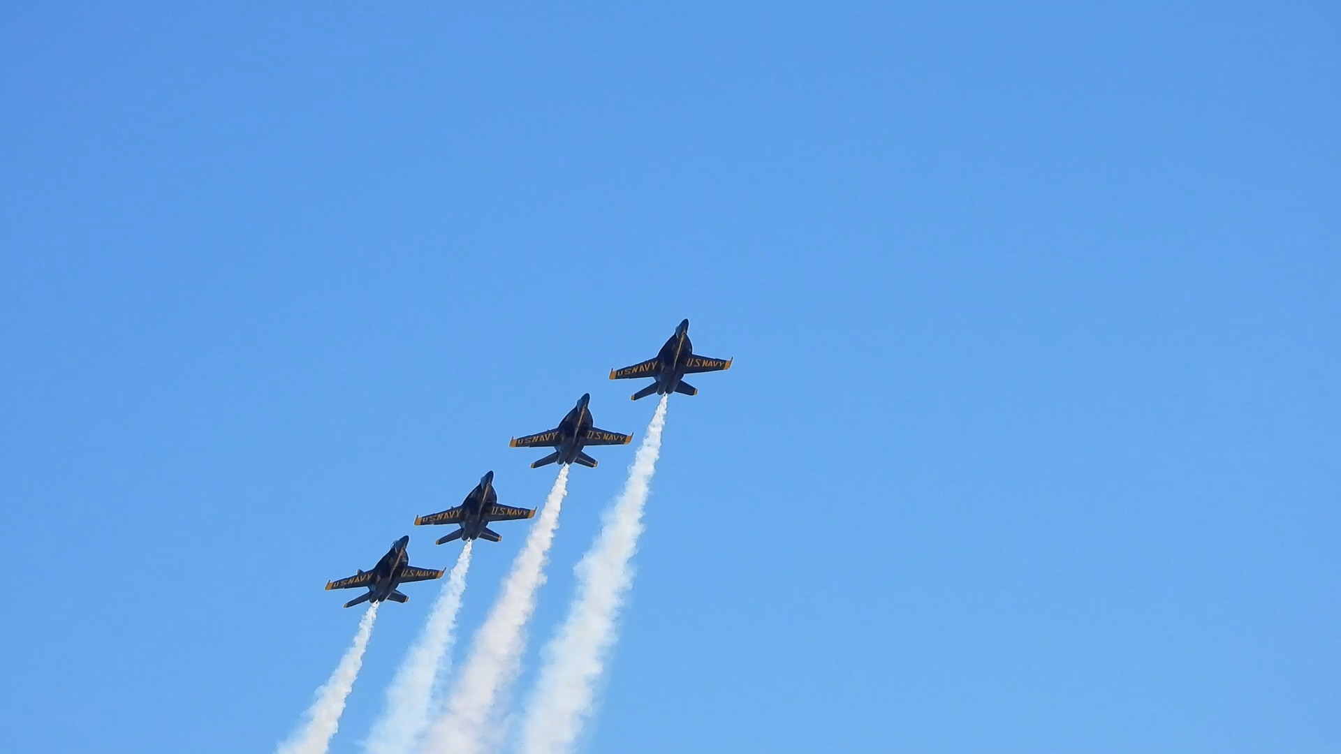 Four jets climb in a staggered line, each trailing a white smoke plume
