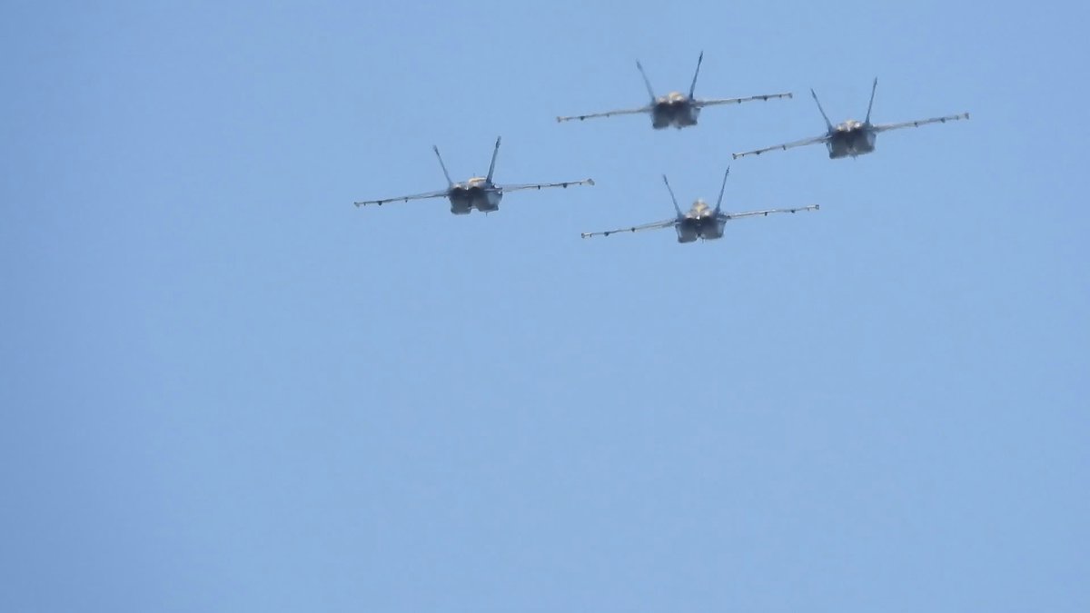 Four jets in formation seen nearly head-on against a pale blue sky