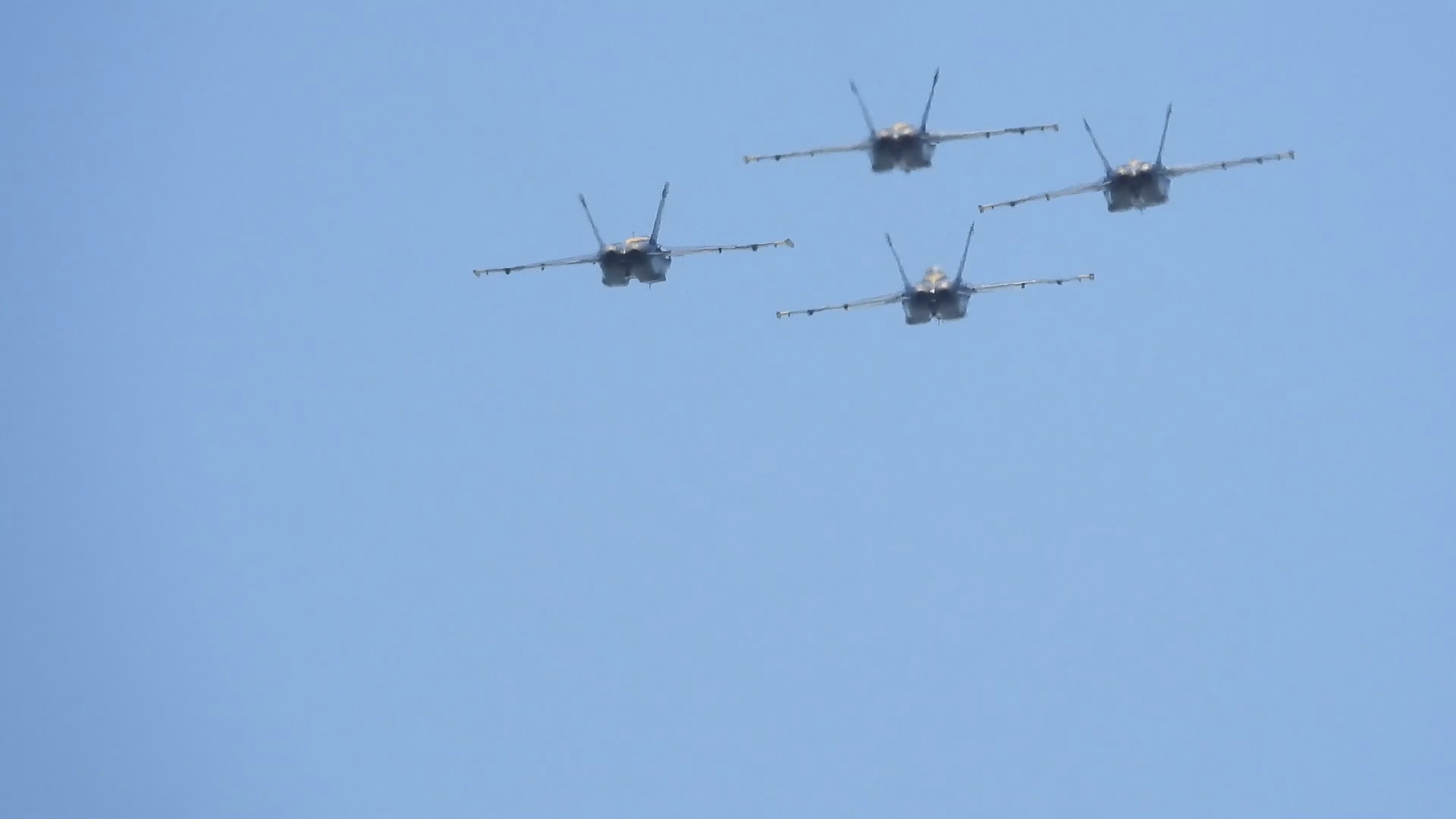 Four jets in formation seen nearly head-on against a pale blue sky