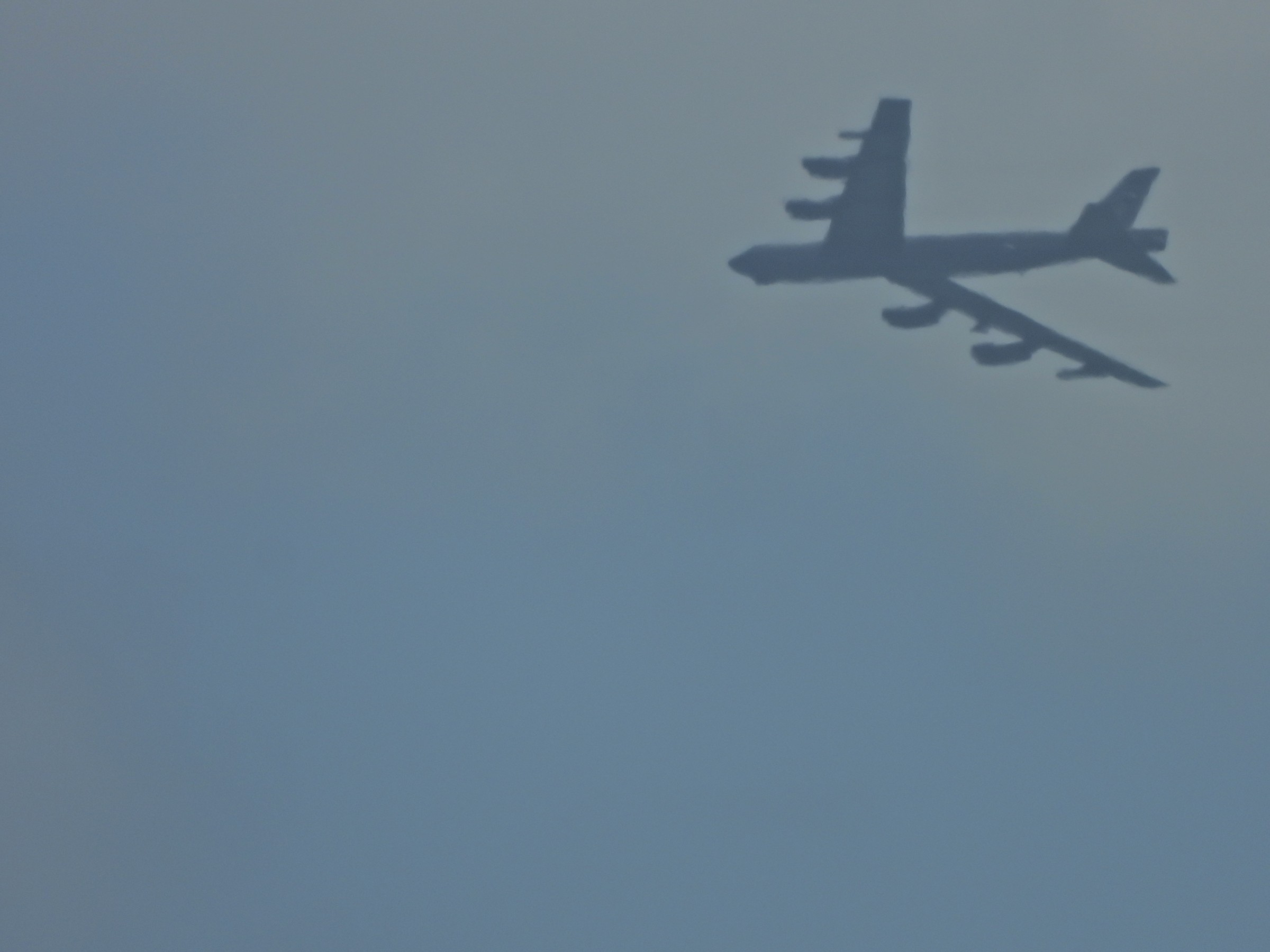 A large eight-engine bomber seen from below against a hazy gray sky