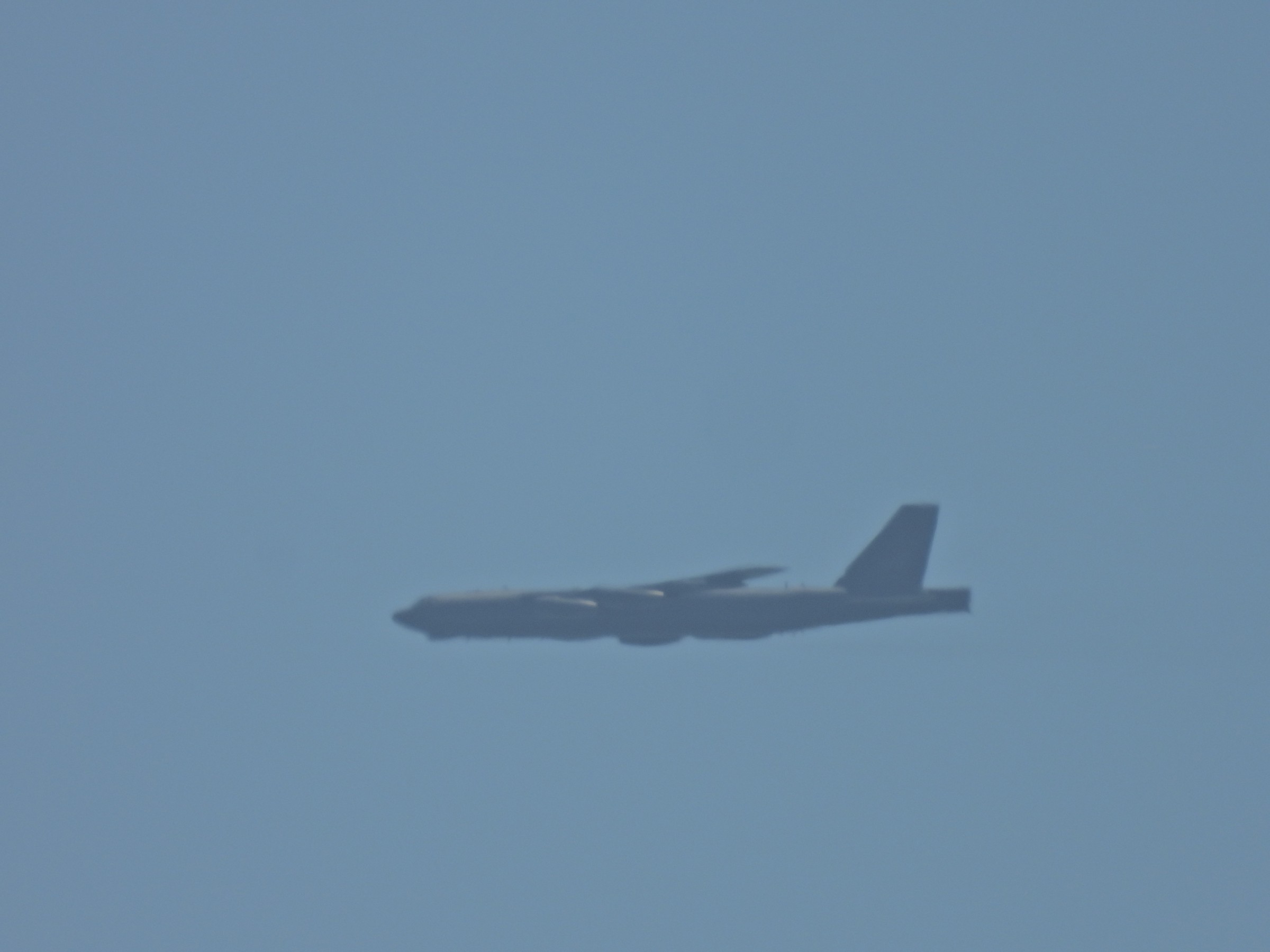 The long side profile of a B-52 bomber in level flight in hazy sky