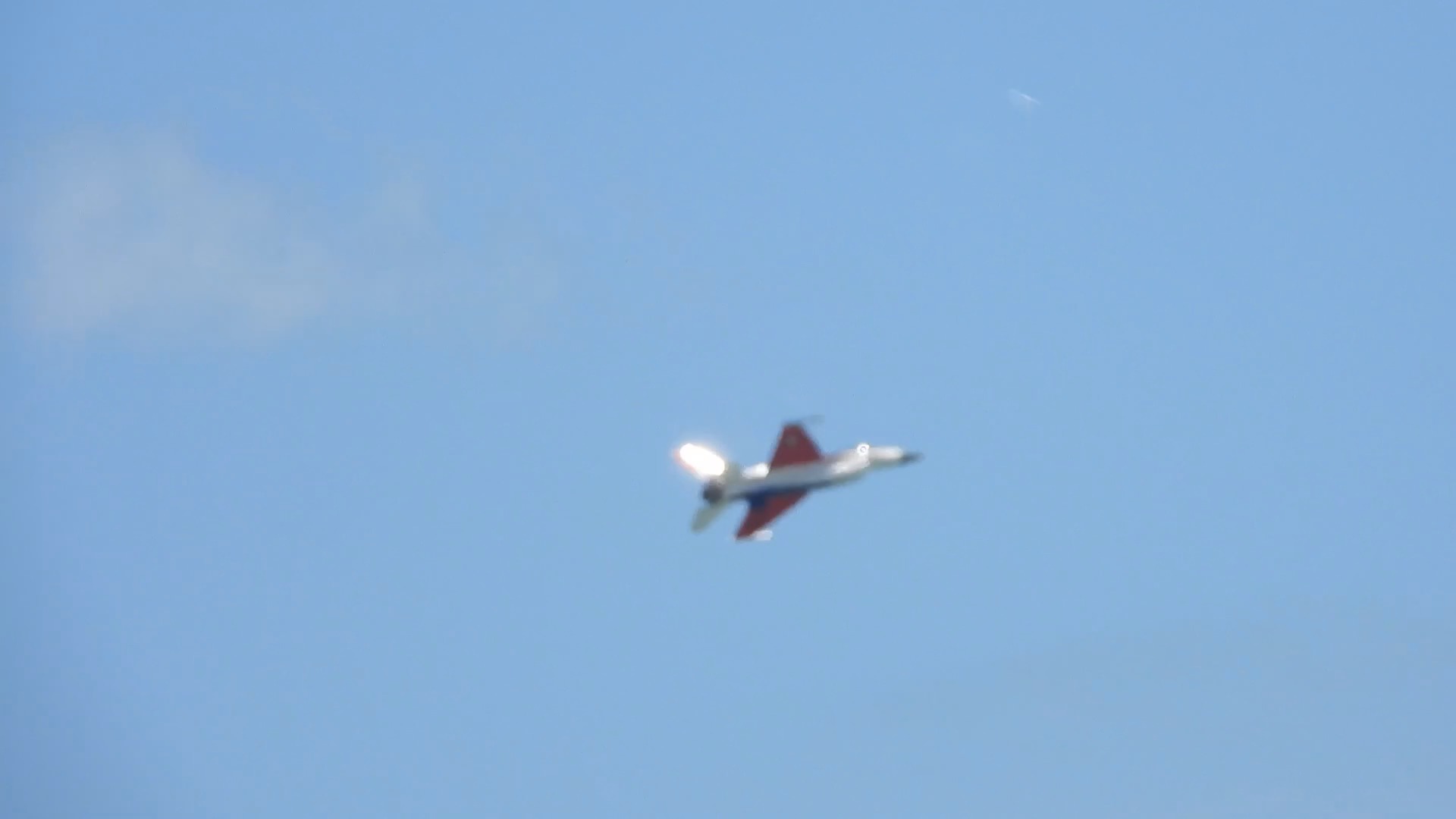 A gray fighter jet with a red-and-white tail flies against a pale blue sky