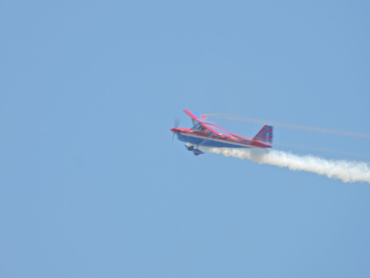 A small red-and-white propeller plane trails white smoke against a blue sky