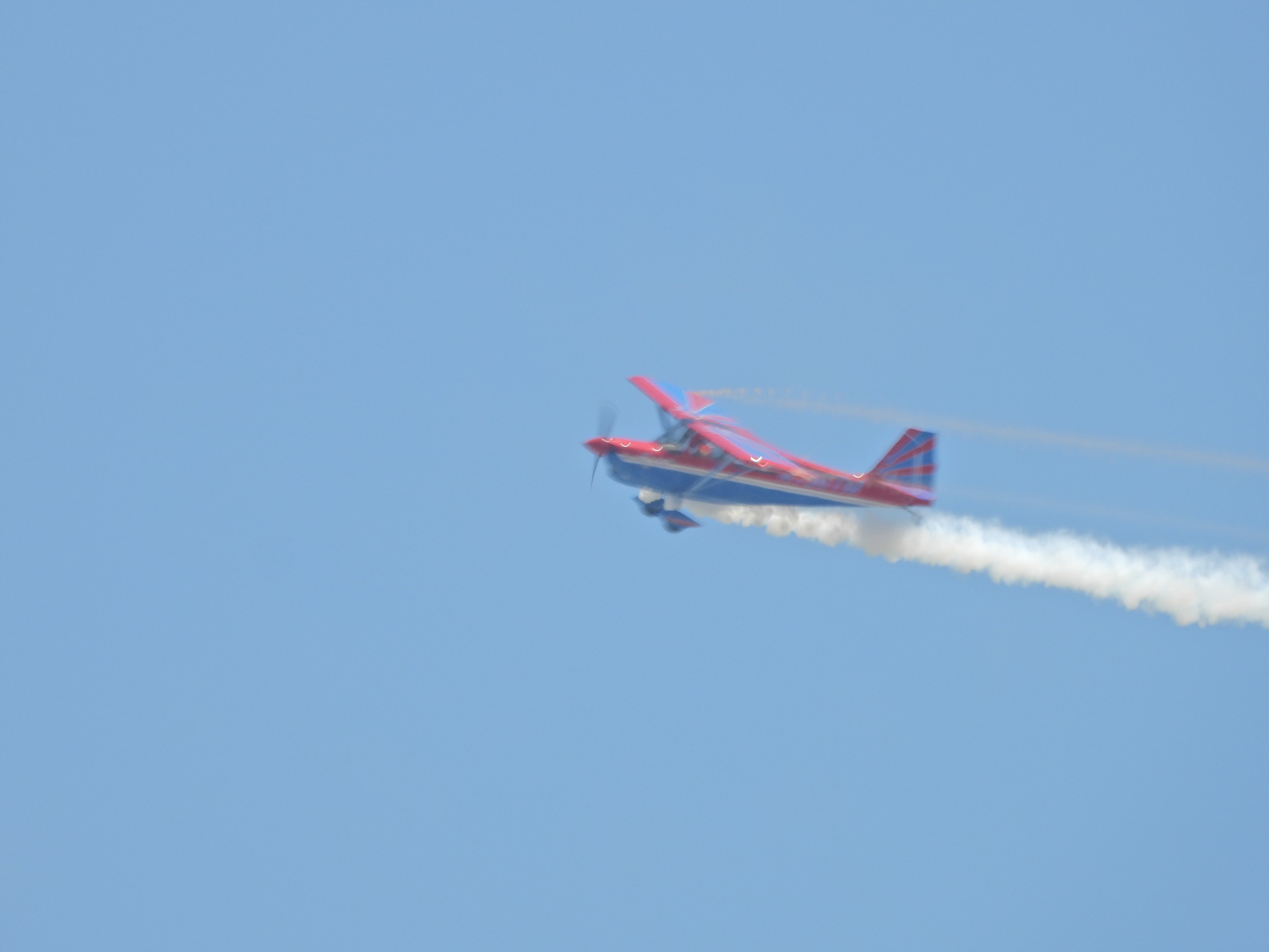 A small red-and-white propeller plane trails white smoke against a blue sky