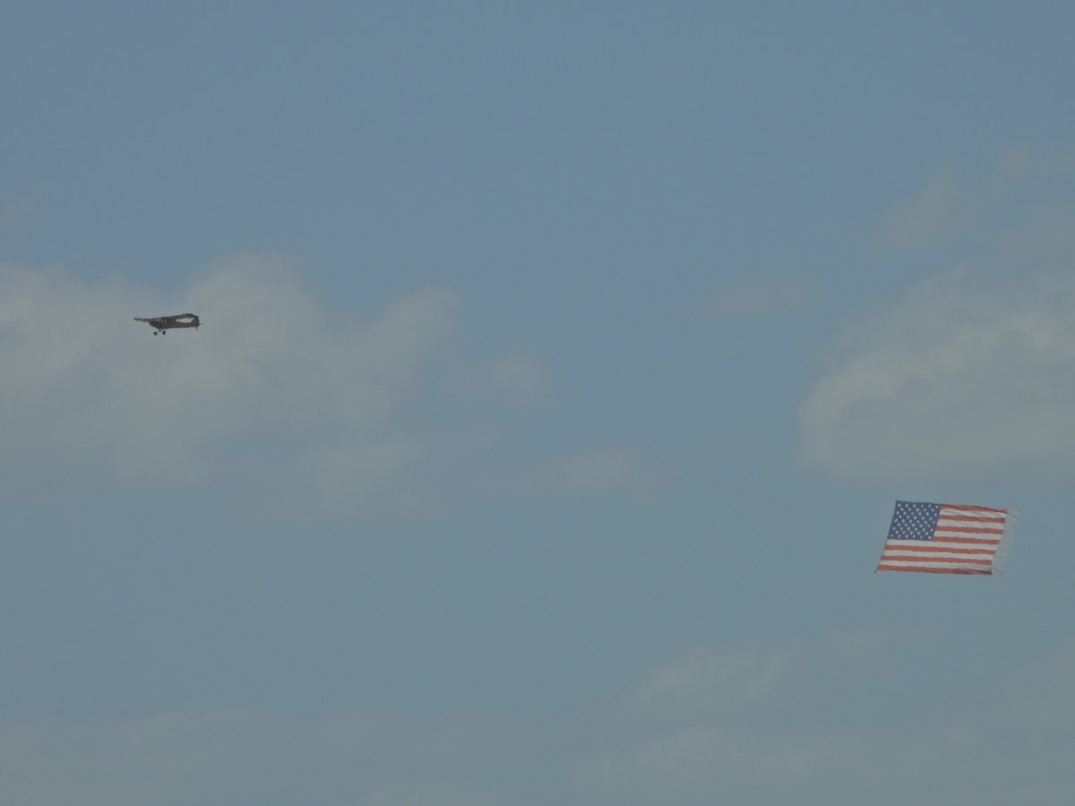 A small plane tows a large American flag banner across a cloudy sky