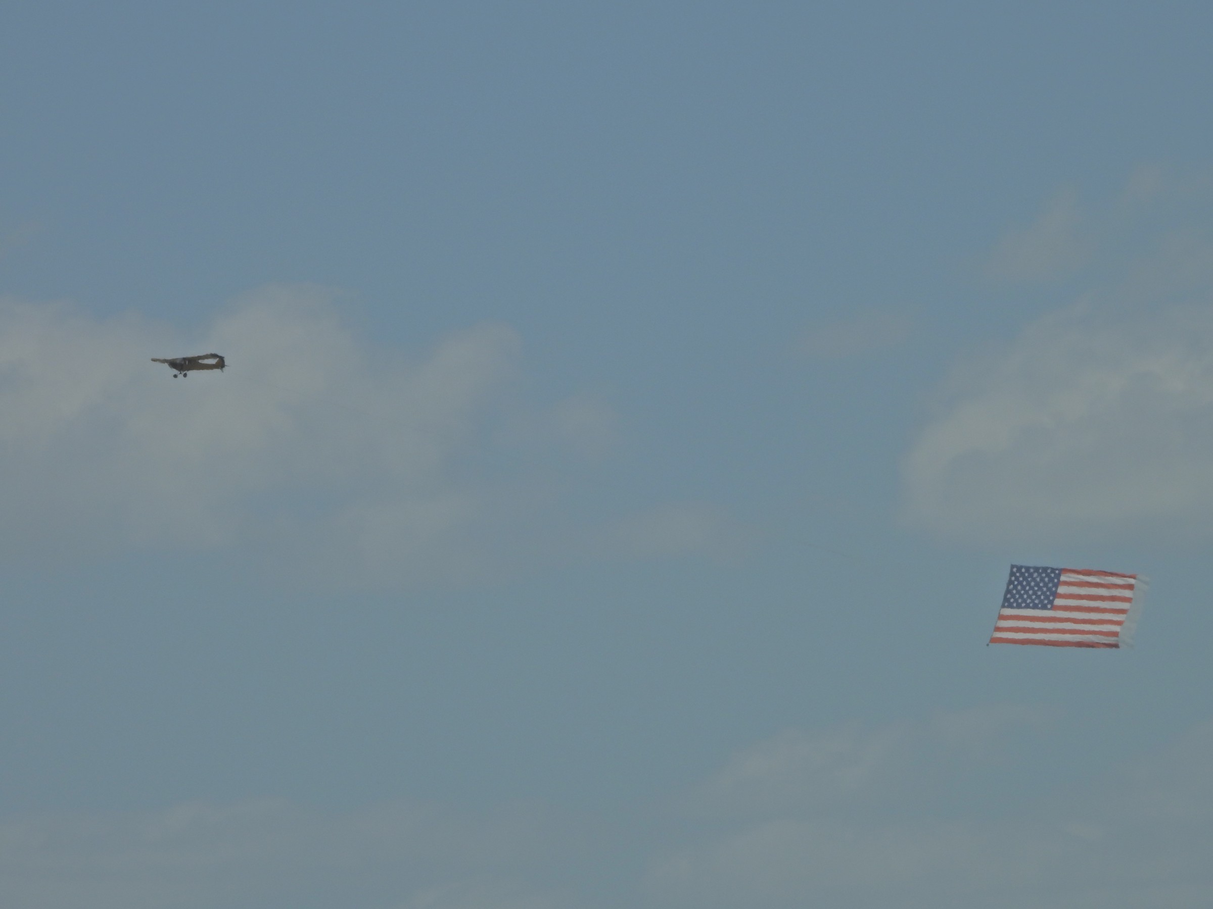 A small plane tows a large American flag banner across a cloudy sky