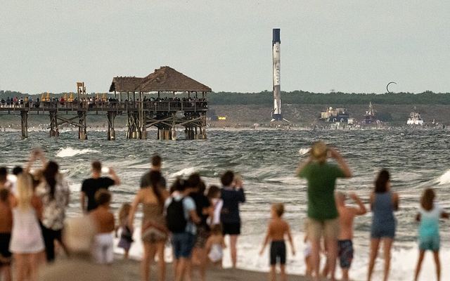 Beachgoers watch a Falcon 9 booster on a droneship being brought into Port Canaveral